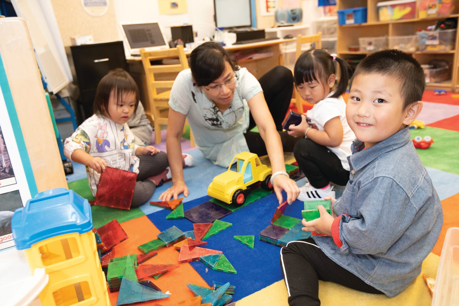 Young children playing with blocks in a classroom with their teacher.